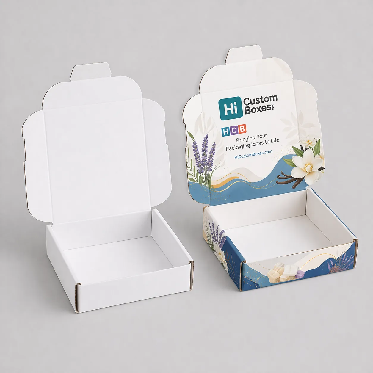 Two open white mailer boxes for wax melts, featuring elegant blue floral illustrations and branding inside. class=